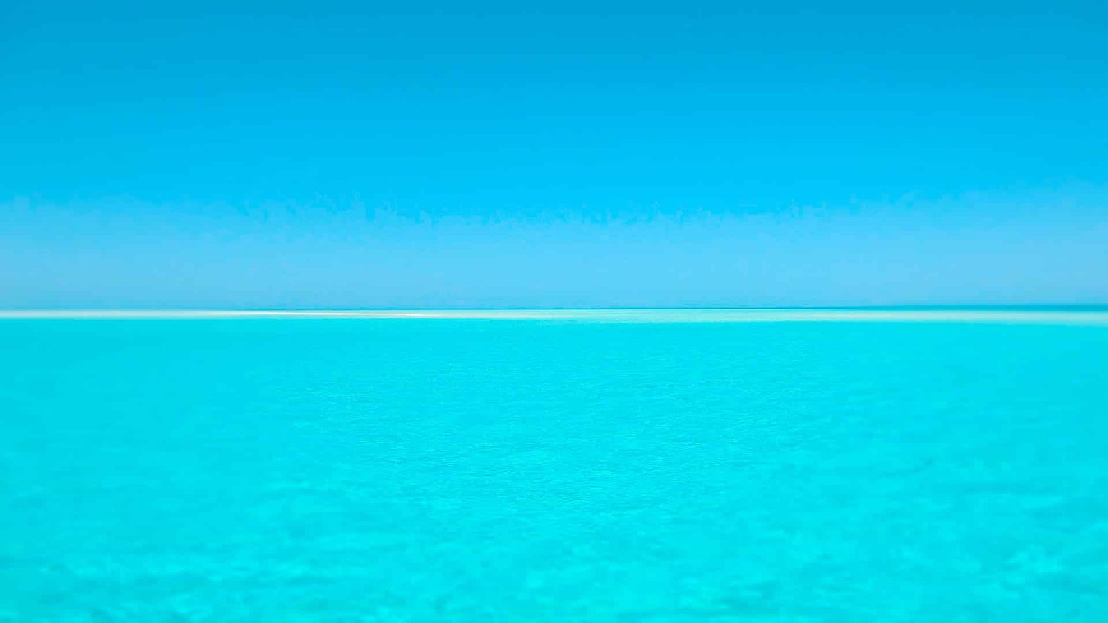 Photographie d'une mer turquoise calme surplombée par un ciel bleu et entièrement sans nuage